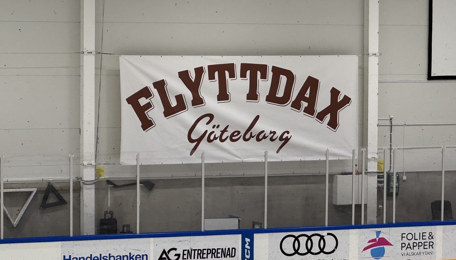 Banderoll med FLYTTDAX Göteborg upphängd bakom glass i en ishockeyrink